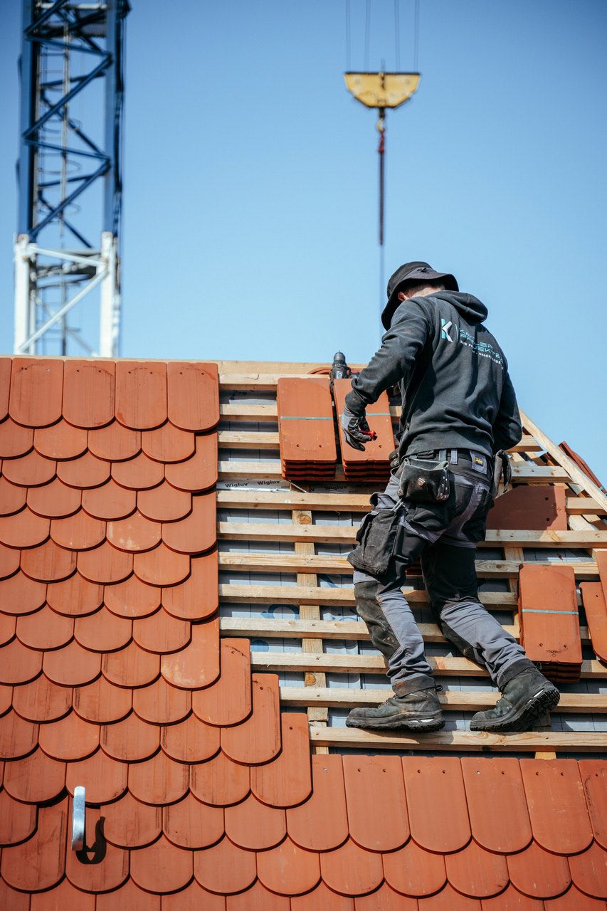 Handwerker deckt ein Dach mit roten Tondachziegeln ein, Baustelle im Raum Stuttgart